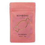 A glossy raspberry-pink packet branded OH MY GUM! sits against a white background. Bright red-pink round bonbons spill out, their shiny surfaces catching light. Bold logo and playful typography top the package, with raspberry illustrations and nutritional text visible. A subtle shadow grounds the scene.