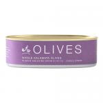 A glossy glass jar of deep purple Kalamata olives sits against a neutral background. The Babylonstoren label wraps around the jar, showing clean typography and subtle olive-branch imagery. Brine glints on the fruit, and a metal lid reflects soft studio lighting. A simple wooden spoon lies beside them.