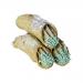 Six Sicilian pistachio cannoli rest on a rustic plate: golden flaky shells brim with pale-green pistachio cream, ends coated in chopped pistachios and a light dusting of powdered sugar; bakery branding sits subtly in the blurred background.