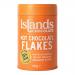 Photograph shows a 200g bag of Islands Chocolate 55% Dark Hot Chocolate Flakes. Transparent window reveals irregular dark brown flakes. A cream-and-brown label displays the brand name, '55% dark' text and an island graphic. The packet rests on a wooden surface with a few flakes scattered. Warm tones