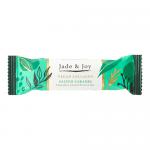 A rectangular 50g bar sits in a glossy bronze and cream wrapper labeled Jade & Joy Vegan Collagen with Salted Caramel text. A partly unwrapped bar shows a dense golden-brown interior streaked with caramel swirls and sprinkled with tiny salt crystals on a clean white background. Subtle embossed logo.