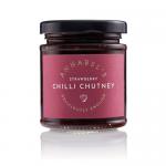 Six small clear glass jars sit in neat rows on a plain surface. Each jar shows glossy, ruby-red strawberry chutney with visible fruit pieces and fine red chilli flecks. White rectangular labels in elegant script and silver screw lids read Annabel’s Deliciously British Strawberry Chilli Chutney. Shot