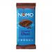 A glossy rectangular chocolate bar lies unwrapped on a wooden board, revealing smooth, rounded squares and a creamy sheen. A torn wrapper with bold NOMO lettering and warm beige and chocolate-brown graphics rests beside it as soft light creates gentle highlights and shadows, and faint cocoa dusting.