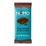 A matte, minimalist wrapper in deep brown and warm beige shows the NOMO logo in bold white. A partially unwrapped dark chocolate block sits beside it, revealing glossy caramel swirls and scattered flaky sea salt crystals on the surface, with a few crumbs on a light background.