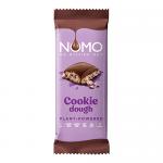 A close-up photograph shows a large NOMO chocolate block bar with a glossy dark-brown surface; one corner is broken to reveal a pale, cookie-dough interior studded with dark cookie crumbs. The partially peeled wrapper displays brown and cream graphics and the NOMO logo. Soft lighting reveals surface.