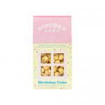 A close-up photograph shows a clear bag of Popcorn Shed Birthday Cake popcorn. Fluffy kernels wear pastel pink and white candy coatings and are dotted with rainbow sprinkles. The package label features playful typography and a small window revealing the colourful contents.