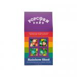 The photo shows a neat arrangement of ten compact packs of Rainbow Popcorn. Each translucent bag reveals vibrant, multicolored popped kernels in shades of red, orange, yellow, green, blue and purple. Bright, playful packaging and scattered loose kernels surround the packs. A glossy sheen gleams afar