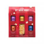 A colorful box with six small tins and sachets sits neatly arranged: a clear bag of popped corn, labeled tins with retro typography, tiny jars of salt, sugar, cheese and caramel powders, and a striped paper bag on a wooden surface under warm light.