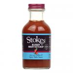 A glossy photograph shows six 300g bottles of Stokes Bloody Mary Tomato Ketchup arranged in two rows of three, their deep red contents visible through clear glass. Labels feature bold black typography, a red tomato illustration and a white cap, set against a pale neutral backdrop. Soft studio sheens