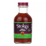 Six glass bottles of Stokes Chilli Ketchup sit upright in a neat row. Each 300g bottle displays a white label with the green Stokes logo, chili illustration and product text. The deep red sauce shows through clear glass, capped by cream-coloured screw lids. Soft gleams catch on glass, labels faintly