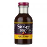 Six identical 325g glass jars sit in two neat rows, each revealing a glossy, dark brown, viscous BBQ sauce through clear glass. Each jar displays a colorful rectangular label bearing the brand name and product title, topped with matching screw-on lids that reflect studio lighting. Soft studio sheen.