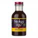 Six identical 325g glass jars sit in two neat rows, each revealing a glossy, dark brown, viscous BBQ sauce through clear glass. Each jar displays a colorful rectangular label bearing the brand name and product title, topped with matching screw-on lids that reflect studio lighting. Soft studio sheen.