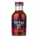 A row of six clear glass bottles stands, each filled with deep red-brown chunky relish. Cream labels encircle the midsection with a bold Stokes logo and product name, accented by simple graphics. Metal screw caps shine as light reflects on the glass surfaces. Neutral backdrop casts soft even shadows.