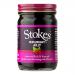 Six clear glass jars sit in a tidy row, each holding deep ruby-red jelly. Silver lids reflect light. White labels display the Stokes logo and simple black text. Light catches the glossy surface of the jelly, revealing smooth, translucent texture and tiny suspended seeds. Thin paper bands around base.