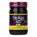 Six clear glass jars of Stokes Sticky Pickle are arranged in two rows; each 430g jar reveals amber-brown chutney studded with mustard seeds and fruit pieces. Cream labels show the Stokes logo with red and gold accents, topped by metal screw lids catching soft studio light. Slight condensation forms.