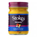 A row of six stout glass jars with golden metal lids displays bright yellow-green piccalilli studded with chunks of vegetables. Each jar has a clean white label featuring the Stokes logo and simple text; condensation and light reflections highlight the glossy, chunky texture on a neutral background