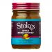 Clear glass jar shows chunky, golden-orange mango chutney. A cream-and-red label wraps the middle with the Stokes name and product text; a dark metal lid closes the top. Visible fruit pieces sit in glossy, spiced syrup and light reflects off the textured surface. Label typography and crest look crisp