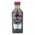 Ten squeezable plastic bottles stand grouped, each with a tapered SQUEEZY shape and red flip-top cap. Transparent bottles reveal glossy dark brown sauce. Each bears a rectangular branded label with clear typography and modest decorative elements, set against a white background. Soft studio lighting.
