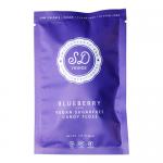 Bright turquoise and purple wrappers encase 12g cones of fluffy, pale-blue candy floss. Playful blueberry illustrations and a clear window reveal airy, spun strands. A small branded label and ingredient panel sit on glossy confectionery packaging in a neat ten-pack arrangement. Light catches fibers.