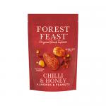A clear snack pouch shows glossy honey‑coated peanuts and almonds flecked with red Serrano chilli, scattered among dried fruit bits and mixed seeds. A colourful Forest Feast label and earthy background complete the close-up, high-contrast food shot.