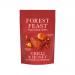 A clear snack pouch shows glossy honey‑coated peanuts and almonds flecked with red Serrano chilli, scattered among dried fruit bits and mixed seeds. A colourful Forest Feast label and earthy background complete the close-up, high-contrast food shot.