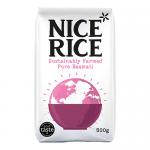A photo shows a cardboard tray holding twelve 500g bags of Nice Rice Pure Basmati, arranged in three rows. Each bag displays the Nice Rice logo and a 'Pure Basmati' label on green-and-white packaging with a clear window revealing long white grains. The scene has soft studio light on a pale backdrop.