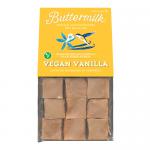 A stack of pale-ivory vanilla fudge squares sits on a white plate, each piece showing smooth, slightly glossy faces and soft, crumbly edges. Tiny vanilla bean specks dot the surface. Warm light creates gentle highlights and soft shadows across the dense, creamy texture.