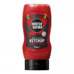 Six 350ml Hunter & Gather chipotle ketchup bottles stand in a neat row against a pale background. Each clear glass bottle shows deep red sauce, black cap and white label with rustic logo and chipotle illustration. Soft shadows and even lighting create a clean, minimalist look. Soft glass reflections