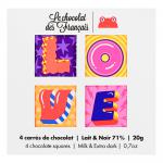 An elegant rectangular gift box opens to reveal twenty square chocolates, each snugly wrapped in colorful, artful paper bearing heart motifs, playful type and French-inspired illustrations. The chocolates form a tidy, vibrant grid inside a clean white tray. Soft shadows fall; a slim ribbon lies on.