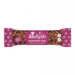 Photo shows a rectangular popcorn bar topped with glossy dark chocolate and scattered almond slivers, resting on a neutral surface beside its cream-and-navy branded wrapper bearing the Joe & Seph’s logo; popcorn clusters are golden and textured, with visible caramel sheen. Soft shadows outline rims.
