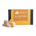 Photo shows an Ozerlat Turkish Delight box in festive red and green Christmas packaging with gold accents. The open tray displays glossy mastic-coated cubes dusted with powdered sugar, neatly arranged beside the branded label and weight marking.