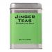 A festive box of Jinger Drinks ginger and mint tea sits on a table, bright red packaging with gold snowflakes and green mint illustrations. A steaming cup, sliced ginger and fresh mint leaves surround a neat row of tea bags beside the box Accents include twinkling lights and a single cinnamon stick