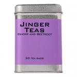 Bright red cartons of Jinger Drinks ginger and beetroot tea sit in neat rows, each box showing stylized beetroot and ginger illustrations, gold snowflakes and holly accents. A steaming glass mug beside them reveals deep pink brew, creating a cozy, festive scene. Soft fairy lights glow; sprigs dusted.