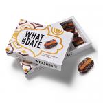 An upright rectangular pack shows bright orange date peels through a clear window. Festive red and gold graphics and holly illustrations frame a central label. The 'What a Date' logo appears above weight information and a small Christmas ornament.