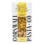 A nest of golden saffron mafalda ribbons sits beside Cornwall Pasta Co packaging. The organic-labelled box features festive Christmas motifs—holly sprigs, gold accents and stars— and is set on a rustic wooden board with warm, soft lighting.