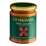 Six 300ml clear bottles of Gymkhana Tikka Masala cooking sauce sit in neat rows on a neutral background. Each bottle shows orange-red sauce, black screw cap and a white label with the Gymkhana logo, 'Tikka Masala' text and decorative spice artwork. Sunlight glints on glass; few spices are scattered.