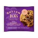 A soft-baked, golden-brown cookie studded with milk chocolate chips shows a central crack revealing glossy hazelnut ganache. Crumbs scatter around its uneven edge; the surface bears toasted specks and molten chocolate pockets that catch the light.