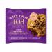 A soft-baked, golden-brown cookie studded with milk chocolate chips shows a central crack revealing glossy hazelnut ganache. Crumbs scatter around its uneven edge; the surface bears toasted specks and molten chocolate pockets that catch the light.