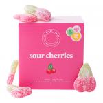 Photo shows a rectangular Ask Mummy & Daddy sour cherries box with bright red cherry illustrations and playful typography. A clear window reveals glossy, individually wrapped deep-red candies. Packaging uses white and pink accents and small nutrition text on the side. Window, light gleams on wrappers.