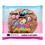 A close-up photo shows a round vanilla cookie studded with glossy, colorful chocolate candies across its surface. Several 50g Kookie Cat Bakery packs with bright, playful branding and a smiling cat logo sit nearby, some slightly overlapping.
