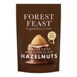 Bright matte wrapper shows stylized firs and deep-green forest graphics with a warm brown band and subtle logo. A milk-chocolate praline bar with whole hazelnuts sits front and center, one segment broken to reveal smooth, nut-speckled filling; six bars line up behind.