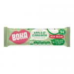 A glossy wrapper displays the Boka logo and Apple & Cinnamon label with warm red and green accents. A golden-brown cereal bar sits beside scattered oats and dried apple pieces, showing oat flakes and a light cinnamon dusting.
