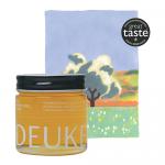 A photo shows six 250g glass jars of Deukes raw monofloral linden honey arranged in two rows. Each jar reveals pale golden honey, a white label with green accents and the Deukes logo, and a gold metal lid that catches soft light on a plain white surface. soft shadows fall behind; tiny bubbles gleam.