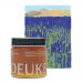Six glass jars of Deukes raw monofloral sage honey sit on a pale wooden surface. Warm amber honey glows through clear glass, viscous swirls catching light. Simple cream labels display brand and floral origin. Background remains soft-focus and neutral-toned. Lids: catch highlights; faint shadows fall.