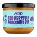 A clear glass jar with a metal lid shows a deep reddish-purple dip inside. The label features bold red and purple graphics with images of red peppers and aubergines and the brand name. A smear of dip and a wooden spoon sit beside the jar on a neutral background.