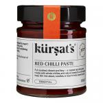 A cluster of twelve 180g glass jars of Kursat's Red Chilli Paste sits on a neutral surface; bright crimson paste peeks through clear glass, textured and glossy. Each jar bears a red-and-white label with the Kursat's logo and simple typography; metal lids reflect studio lights. They sit in neat rows.