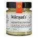 A clear glass jar of Kursat’s preserved lemon paste sits centered on a neutral background. The bright, glossy yellow paste shows flecks of rind and a slightly coarse texture. A blue-and-white label with cursive logo and weight wraps the jar; a metal lid seals it. Soft reflections appear on the glass