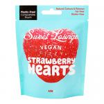 A clear pouch displays bright pink heart-shaped strawberry sweets with a fizzy sugar coating. The Sweet Lounge logo appears on a pink header, and playful fruit illustrations plus vegan and recycling icons border the bag. The pouch has a resealable zip against a white backdrop. Soft shadows frame it.