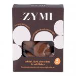 A clean product photo shows a neat packet of Zymi Organic biscuits; several round golden biscuits sit beside the pack, each streaked with dark chocolate and sprinkled with flaky sea salt. A tahini drizzle and the Zymi Bakery logo appear on the wrapper. Warm lighting highlights crumb detail and gloss.
