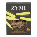 A green-and-white packaged display shows round organic bites studded with flax, sunflower, and pumpkin seeds. The label features the Zymi logo, seed illustrations and weight. Several bites sit loose beside the open pack, revealing a crunchy, seed-dotted surface. soft tones, clear plastic window view
